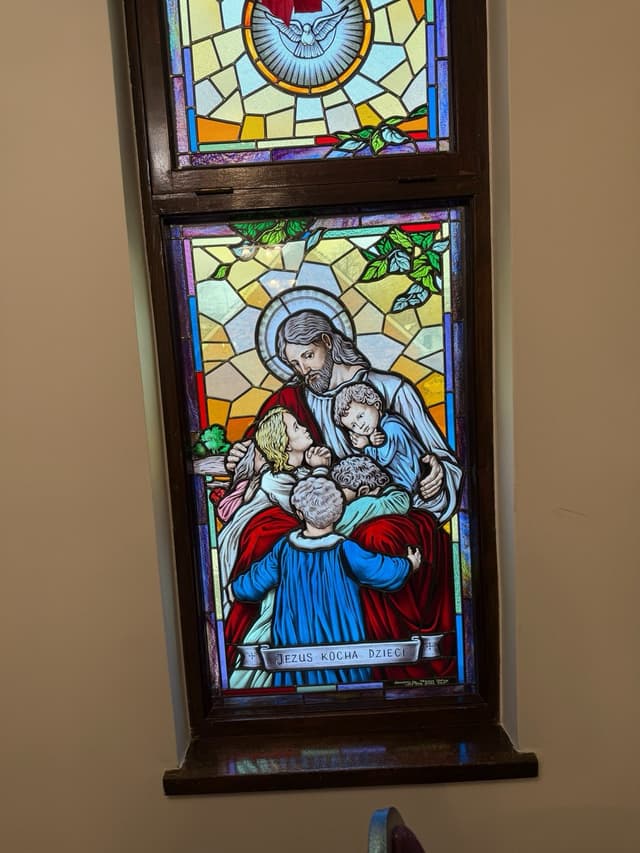 Stained glass window of Jesus embracing children with the Holy Spirit dove above