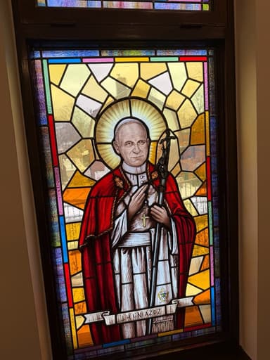 Stained glass window of St. John Paul II in red papal robes holding a crucifix
